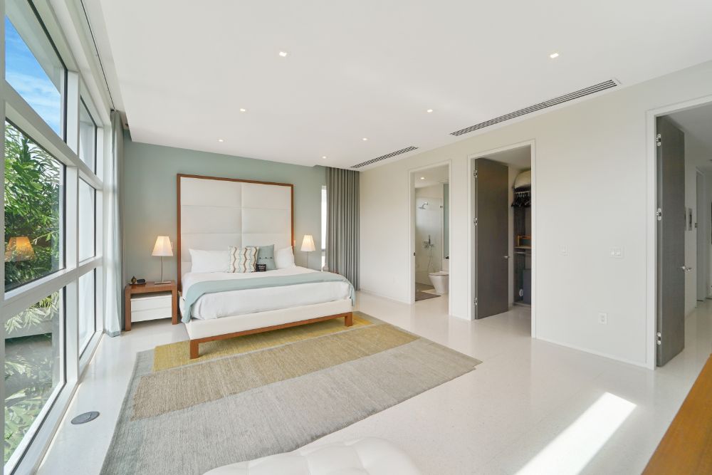 卧室有簇绒床头板，木边桌，侧灯，和一面玻璃墙