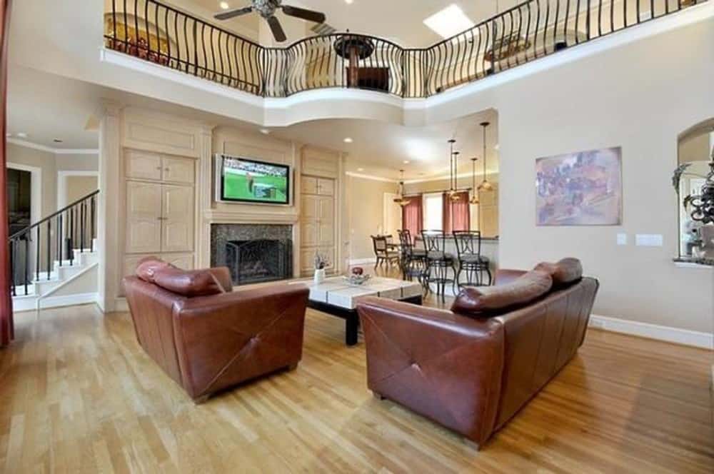 家庭房间有棕色真皮座椅,一个木制的咖啡桌,顶部设有一个电视和一个壁炉。