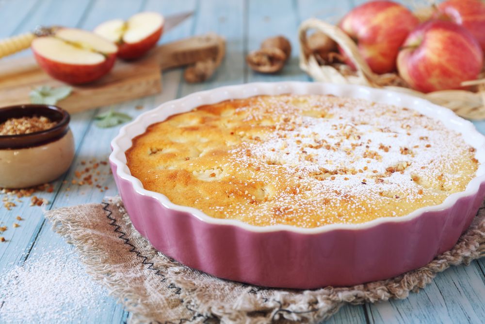 法国苹果蛋糕粉深盘与苹果在背景在木桌上