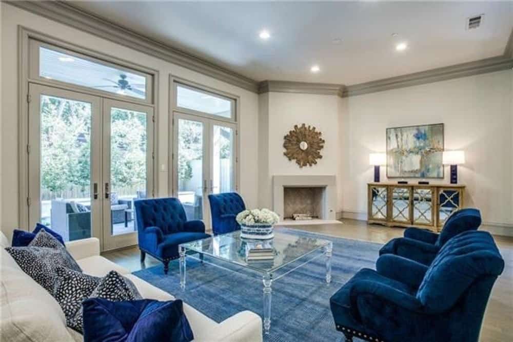 家庭娱乐室以蓝色和白色的调色板为特色，展示了簇绒扶手椅、大面积地毯和角落壁炉，壁炉上装饰着时钟。
