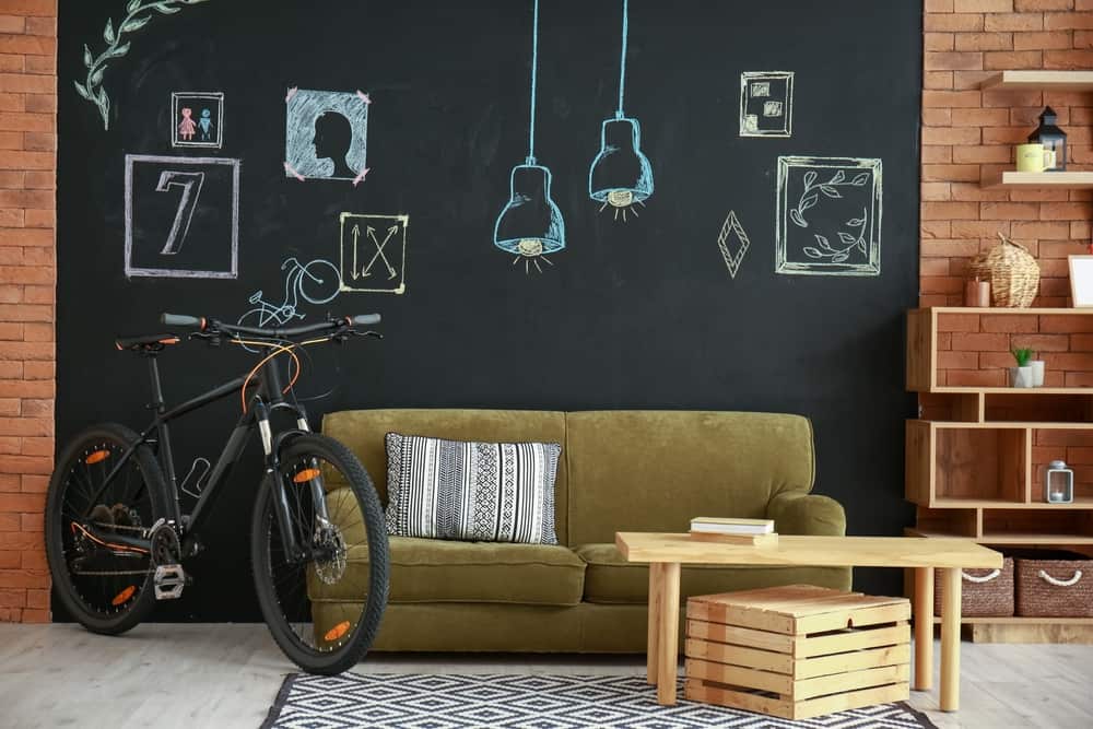 客厅里有一张橄榄绿的沙发、一张木桌、一辆自行车和一面黑板墙。