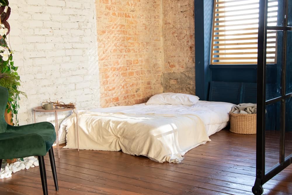 深蓝色砖墙的卧室，硬木地板上铺着床垫。