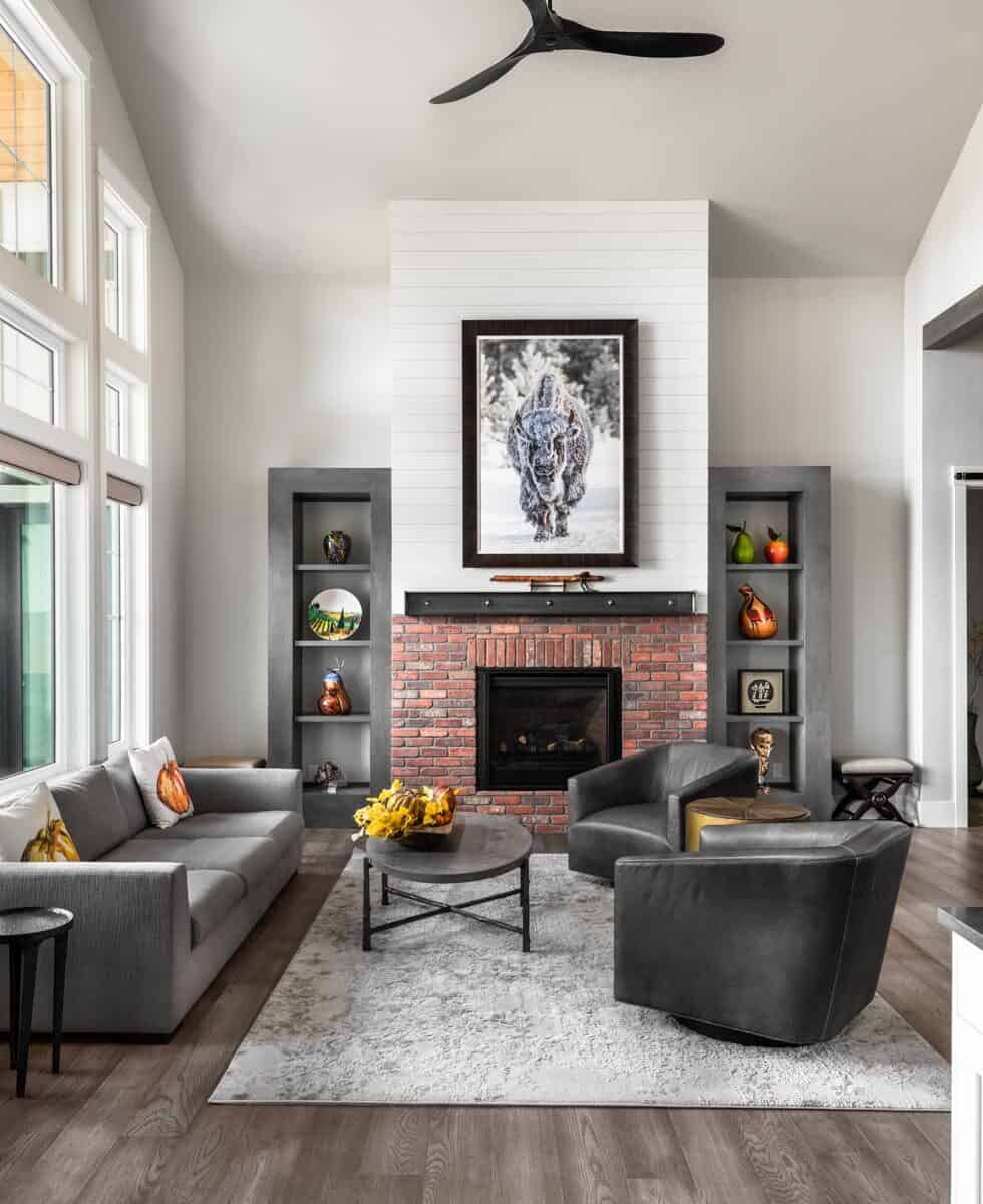 家庭娱乐室里有灰色组合家具、皮革扶手椅和一座砖砌壁炉，壁炉两侧有嵌壁式架子。