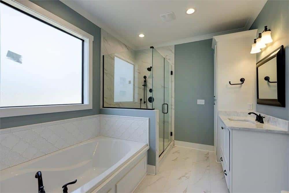 主浴室带有白色梳妆台，一间步入式淋浴房，以及一间靠落地窗采光的浴缸。