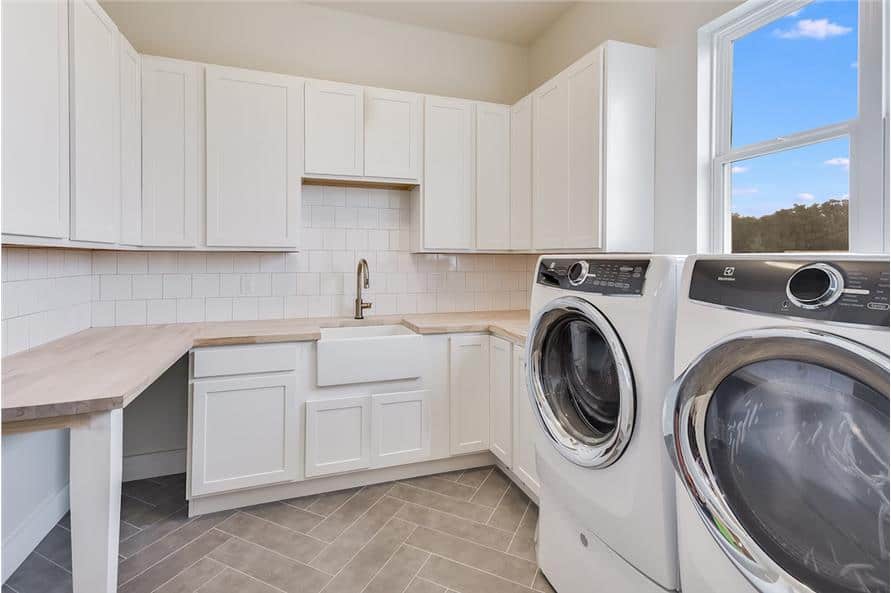 洗衣房配有前置洗衣机和烘干机，白色橱柜，木制台面，和一个实用水槽。