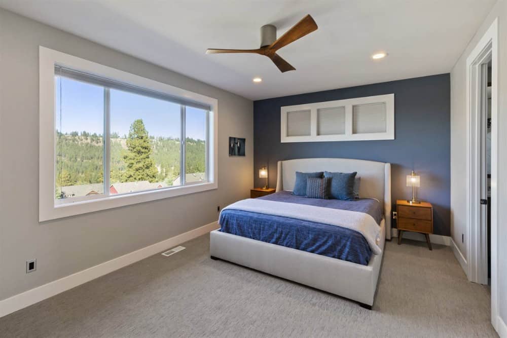 主卧室有一面蓝色的墙壁，一张灰色的软垫床，木制床头柜被温暖的台灯照亮。