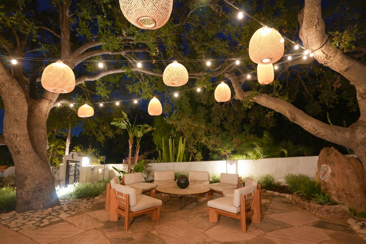 室外生活区有一张圆桌和软垫沙发，坐落在橄榄树中，并被灯笼照亮。