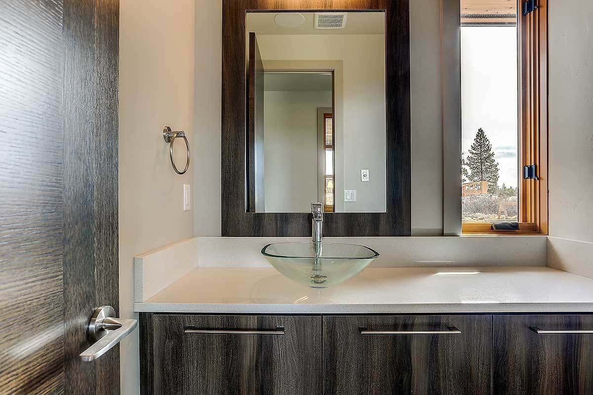 这间浴室设有一个深色的木质梳妆台，上面有一个玻璃器皿水槽和镜框镜子。