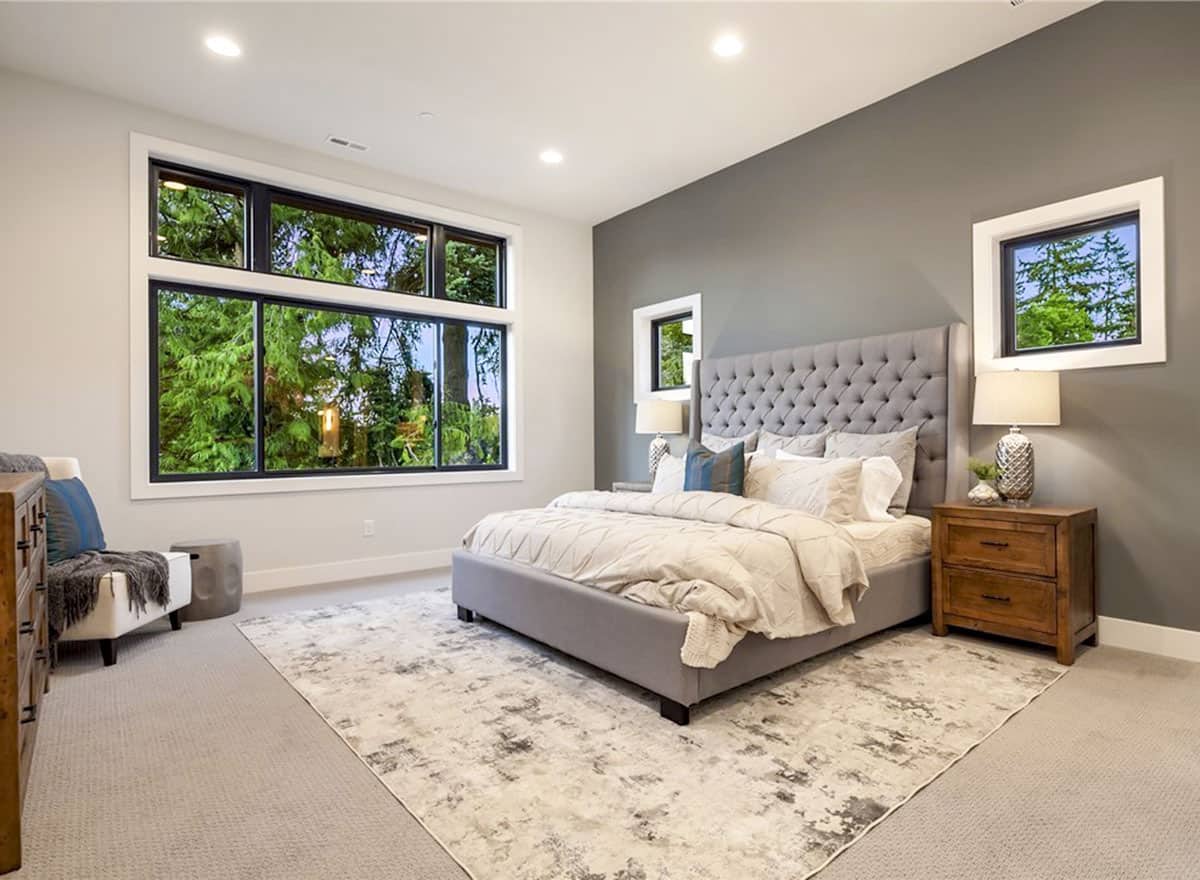 主卧室铺着地毯，一张灰色的簇绒床，两侧有木制床头柜和观景窗。