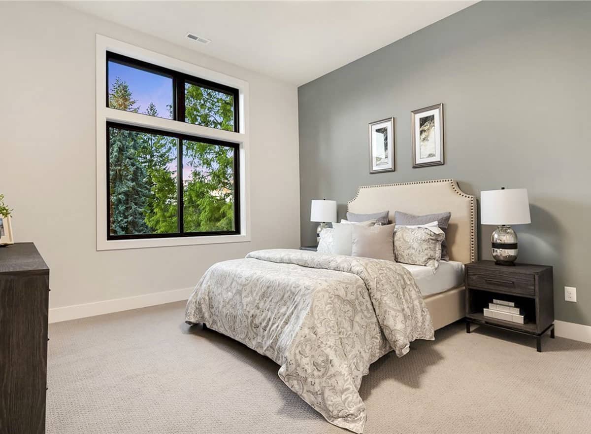 这间卧室以灰色的墙壁和米色的软垫床为特色，配有装裱的艺术品。