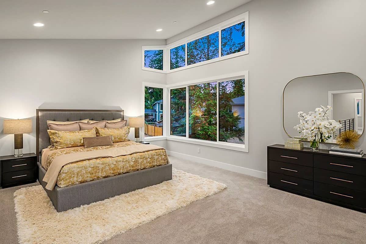 主卧室有一个棚顶天花板，一张灰色的簇绒床，还有大量的窗户，可以让自然光进来。