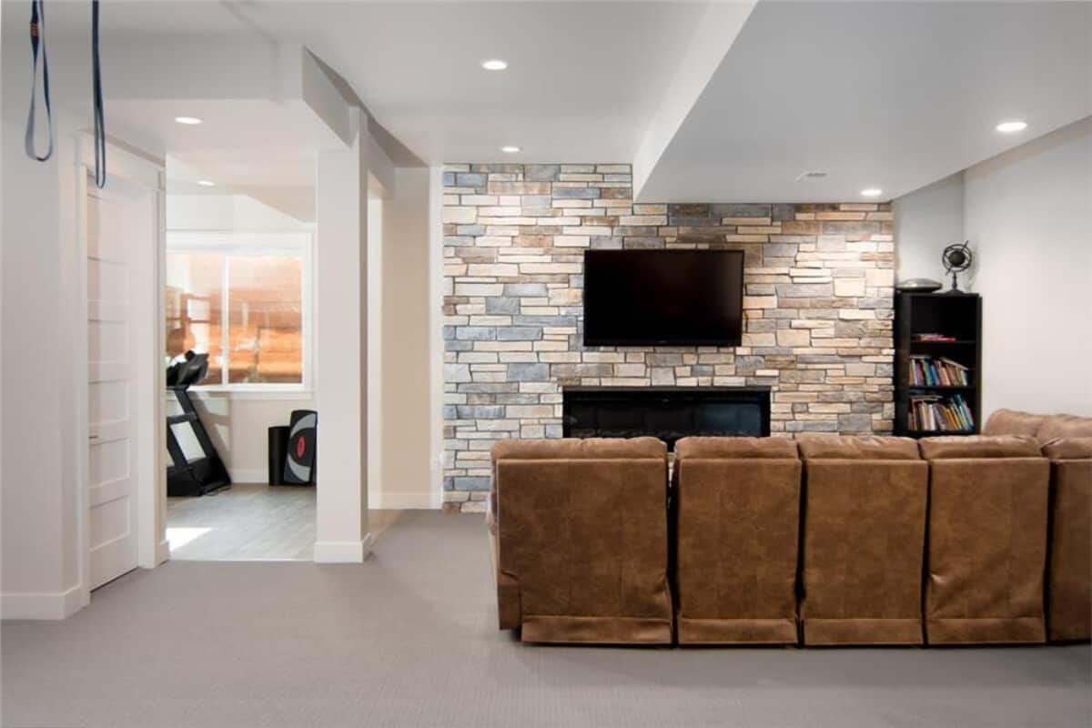 家庭娱乐室，有棕色皮沙发，壁挂式电视，壁炉安装在砖墙上。