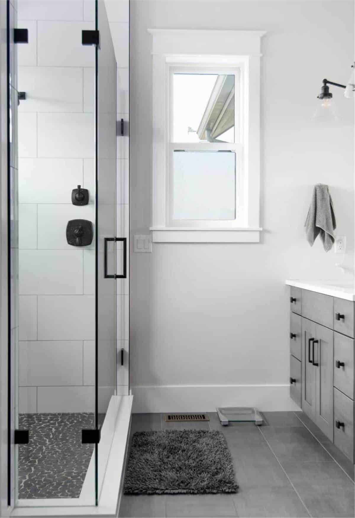 这间浴室有一个灰色的梳妆台，一间步入式淋浴间，还有一扇白色框窗，可以让自然光照进来。