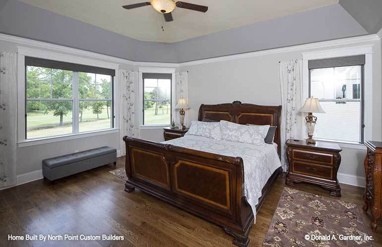 主卧室里有木制家具、一张储物凳和一个装有风扇的拱形天花板。
