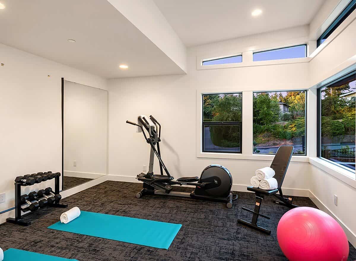 设备齐全的健身房，铺着地毯，有很多窗户。