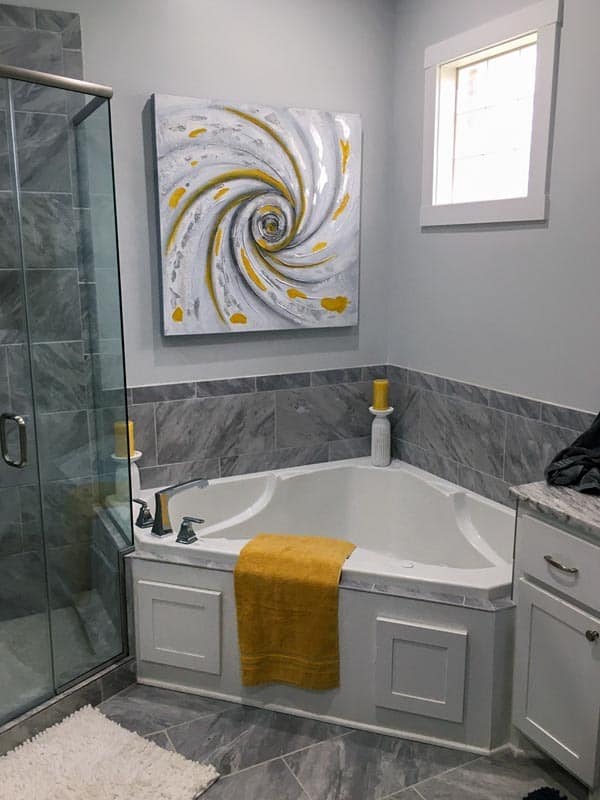 角落里的浴缸装饰着漩涡艺术品，坐落在步入式淋浴间和梳妆台之间。