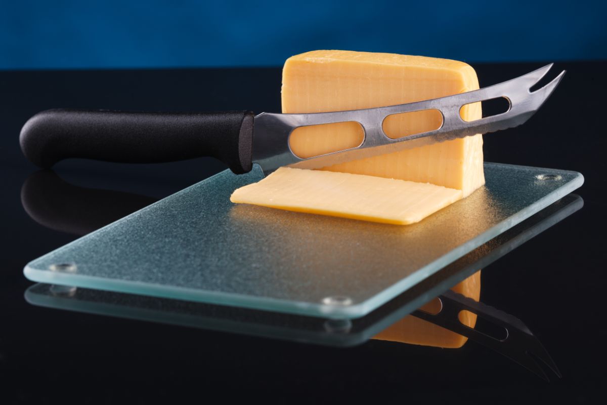 一把刀，切片奶酪放在玻璃砧板上。