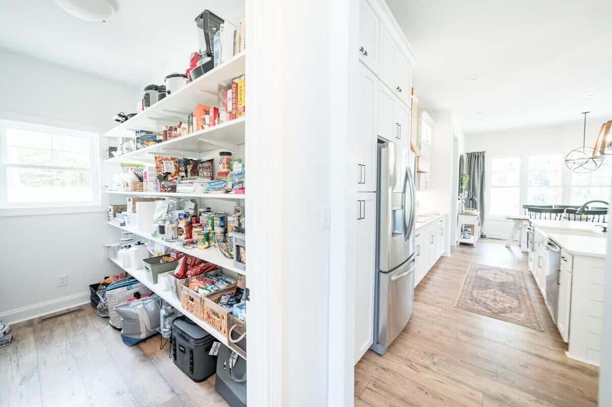 一个带有白色嵌壁式架子的步入式食品储藏室使厨房更加完善。