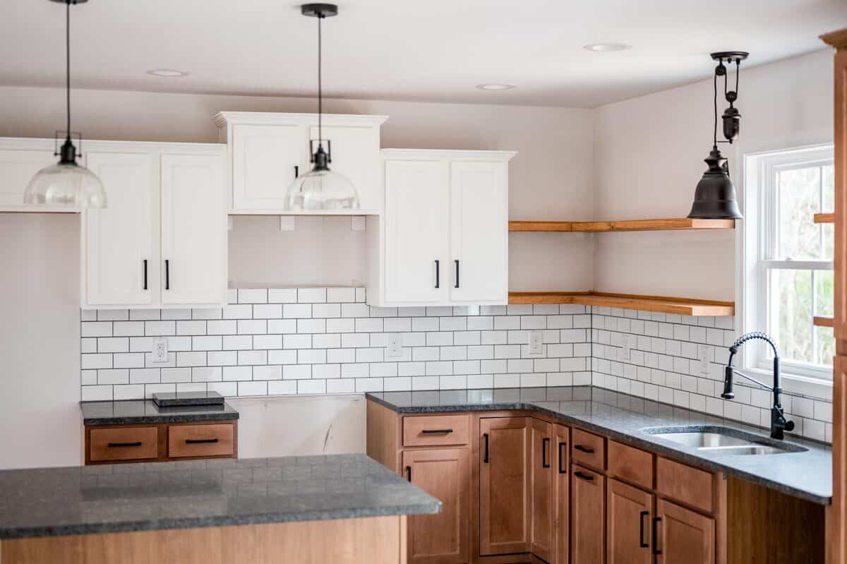 厨房里有对比鲜明的白色和木质橱柜，双水槽，以及安装在白色地铁瓷砖后挡板上方的浮动架子。