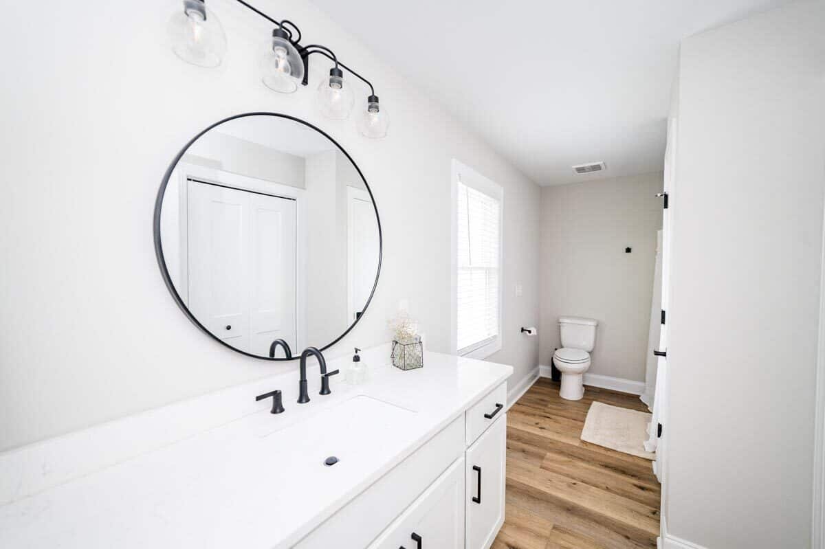 主浴室有一个厕所区和一个白色的梳妆台，上面有一面圆形镜子和玻璃烛台。