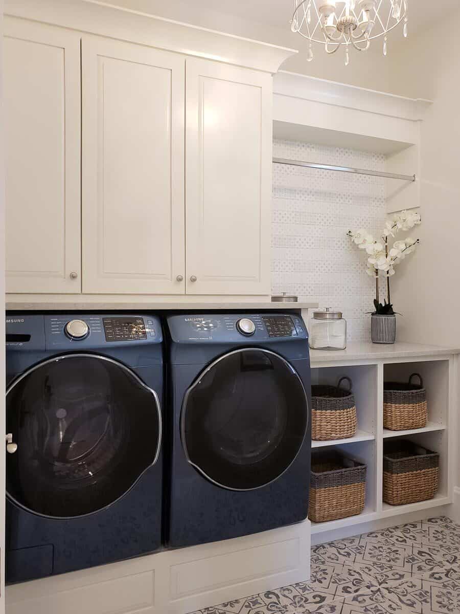 洗衣房有前置电器、白色橱柜和摆满柳条篮子的储物架。