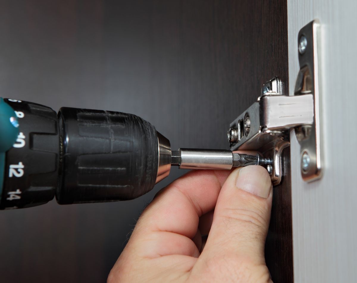 一个人用电钻用螺丝拧门铰链。
