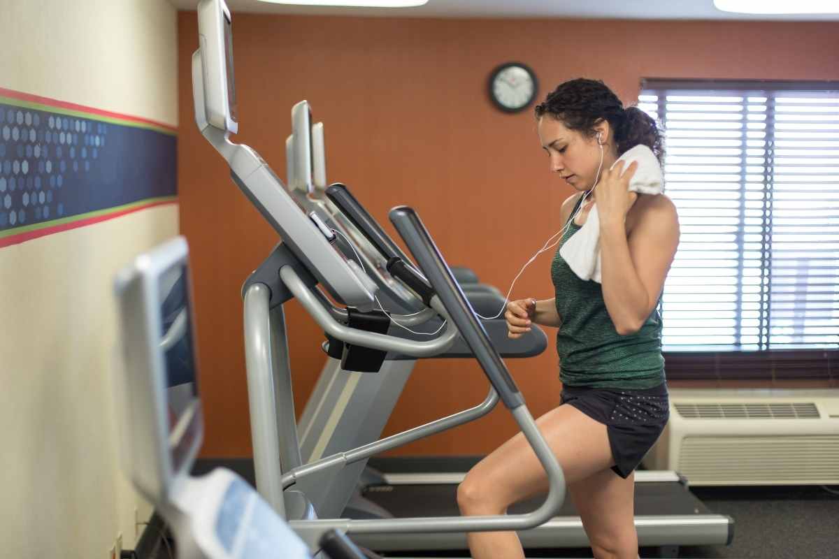 一名女子在健身房的楼梯机上锻炼，同时戴着耳机看数字手机。