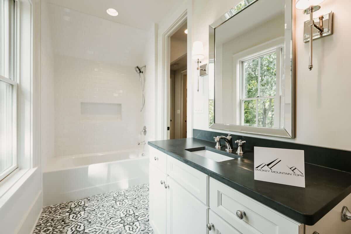 这间浴室配备了大洗手台和浴缸和淋浴组合。装饰瓷砖地板为白色浴室增添了趣味。