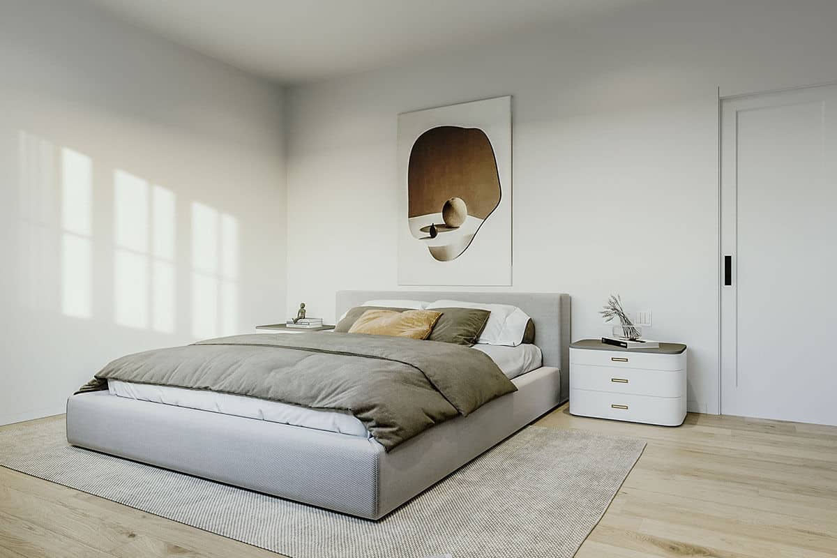 主卧室有一个灰色的平台床，现代床头柜，和可爱的艺术品装饰着鲜明的白色墙壁。