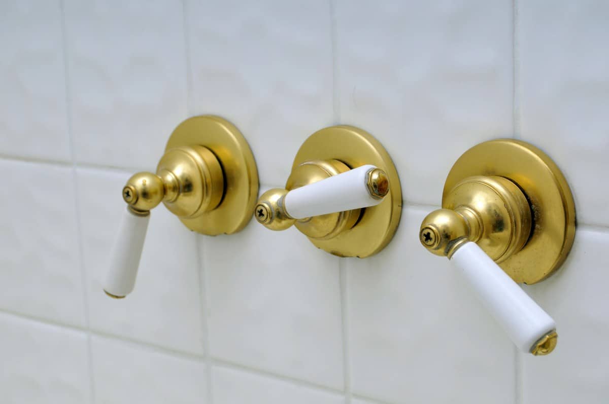 三个黄铜淋浴阀手柄安装在瓷砖墙上。