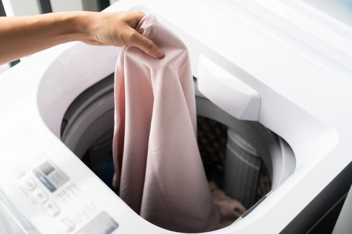 一只手把衣服放在洗衣机上。