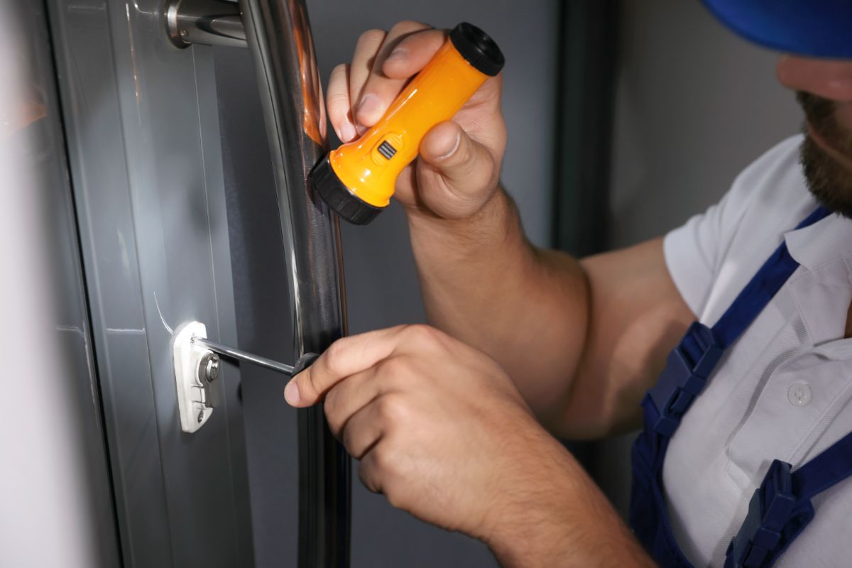男人修理门使用螺丝刀和一个手电筒。