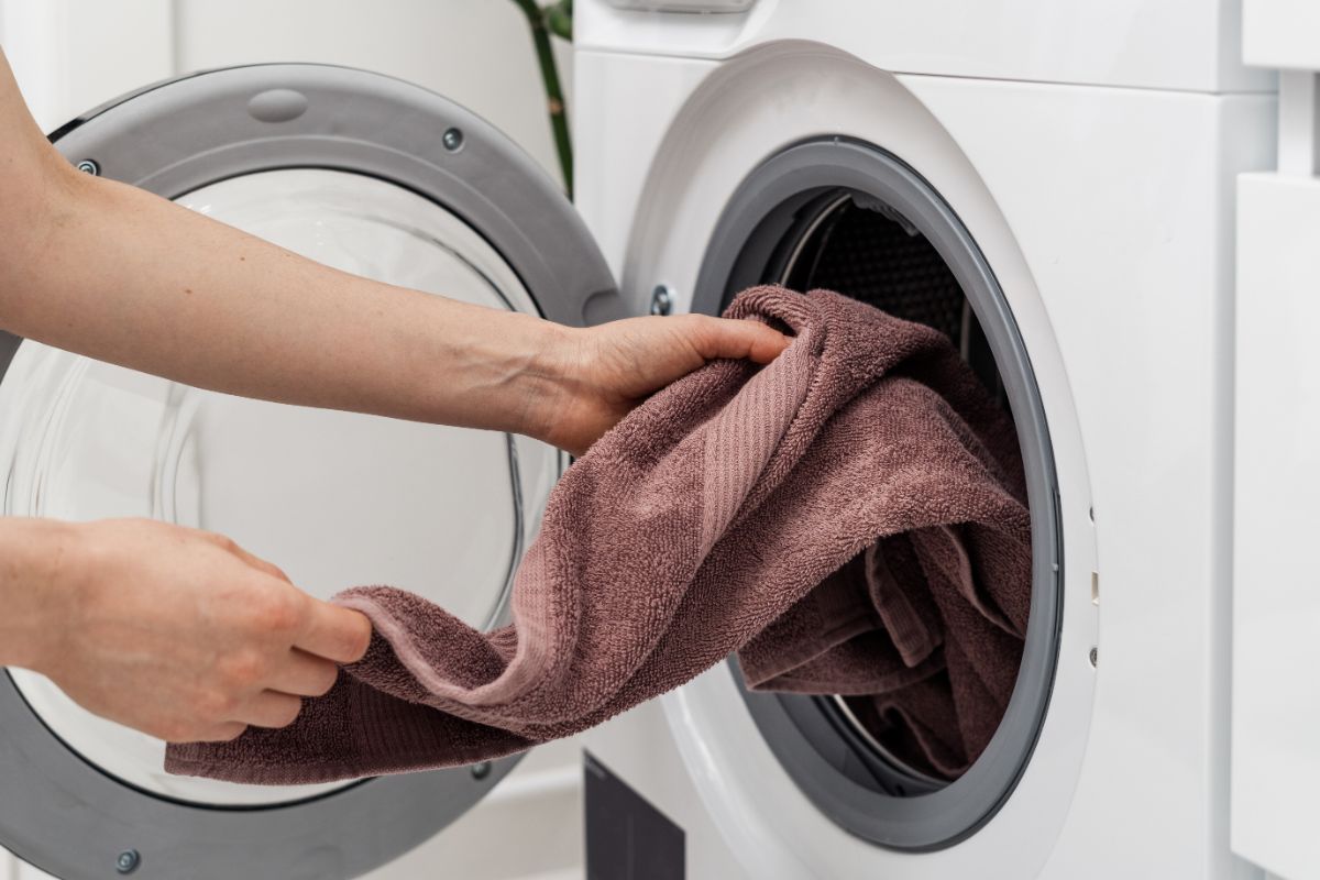一位女士从自动洗衣机滚筒中取出崭新的干净毛巾的裁剪图像。