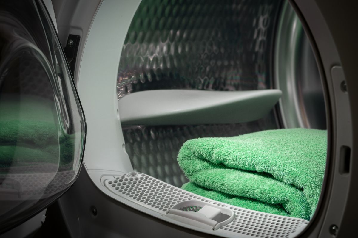 绿色毛巾在洗衣机或滚筒式烘干机里，门开着。