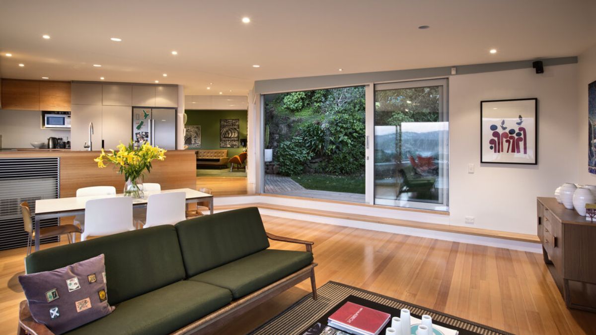 简约的室内客厅的照片在Seatoun山庄的房子,有一个突出的滑动玻璃门,提供一个视图周围的绿色植物。