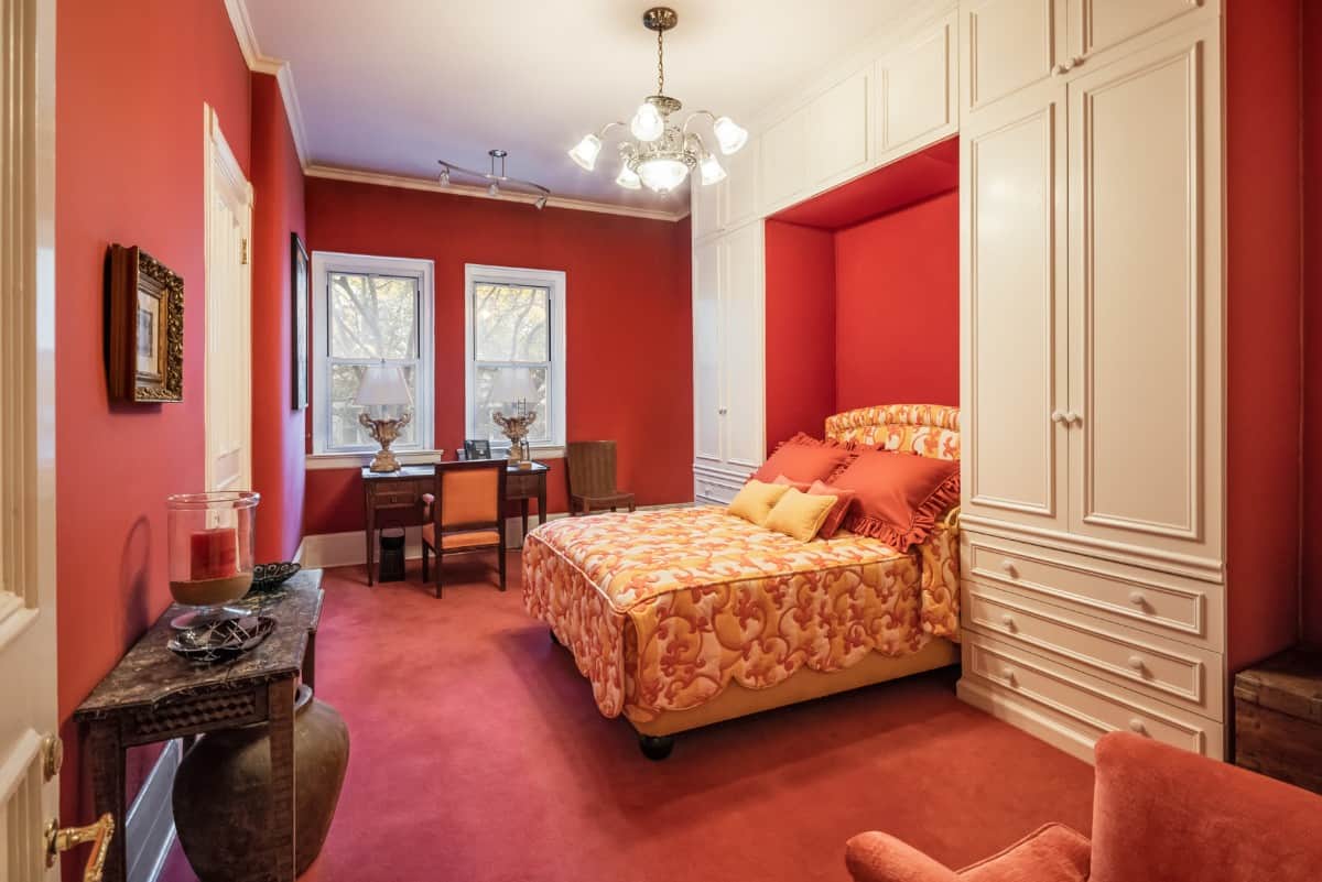 另一间别致的卧室有红墙，配套的地毯地板，床周围有一个内置衣柜。