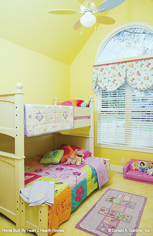 孩子们的卧室，有一张双层床，明亮的黄色墙壁，还有一扇顶有拱形横梁的大窗户。