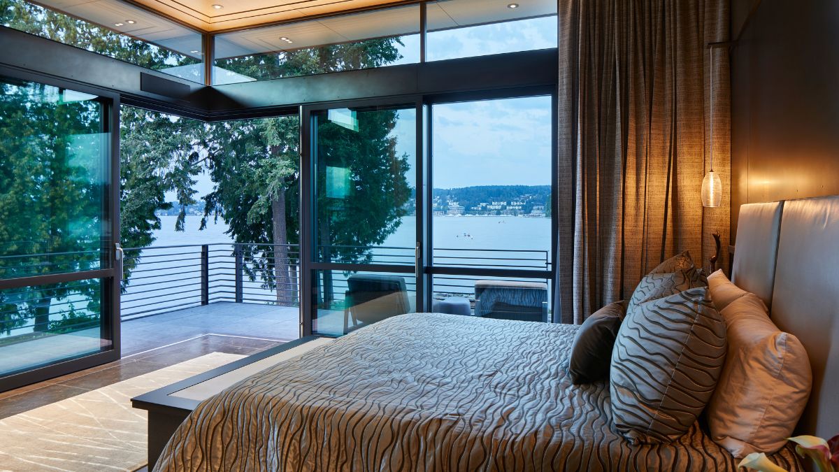 这间卧室有一张大床，现代外观的窗帘，玻璃墙，和一个阳台的看法。