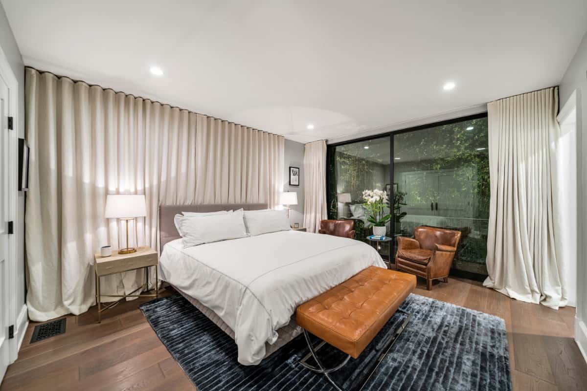 这间卧室提供真皮座椅，一个舒适的平台床，和落地窗穿着米色窗帘。