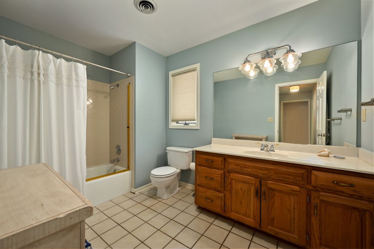 浴室里有一个嵌壁式浴缸，带窗帘保护隐私，还有一个带瓷砖台面的梳妆台。